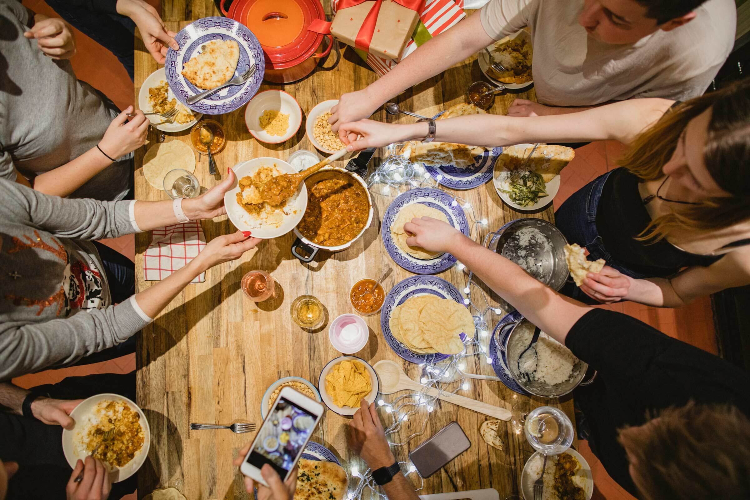 An over-head shot of a table filled with food and surrounded by hungry family members.