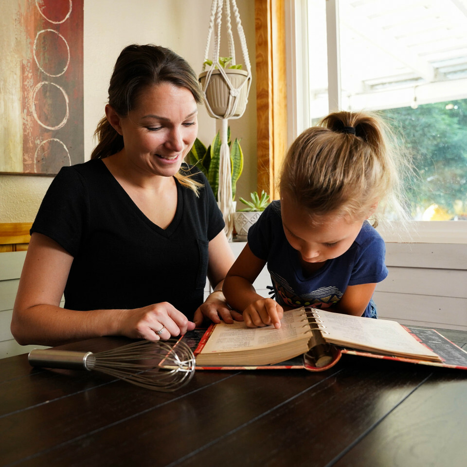 A woman and her daughter look at a cookbook together, ready to bake