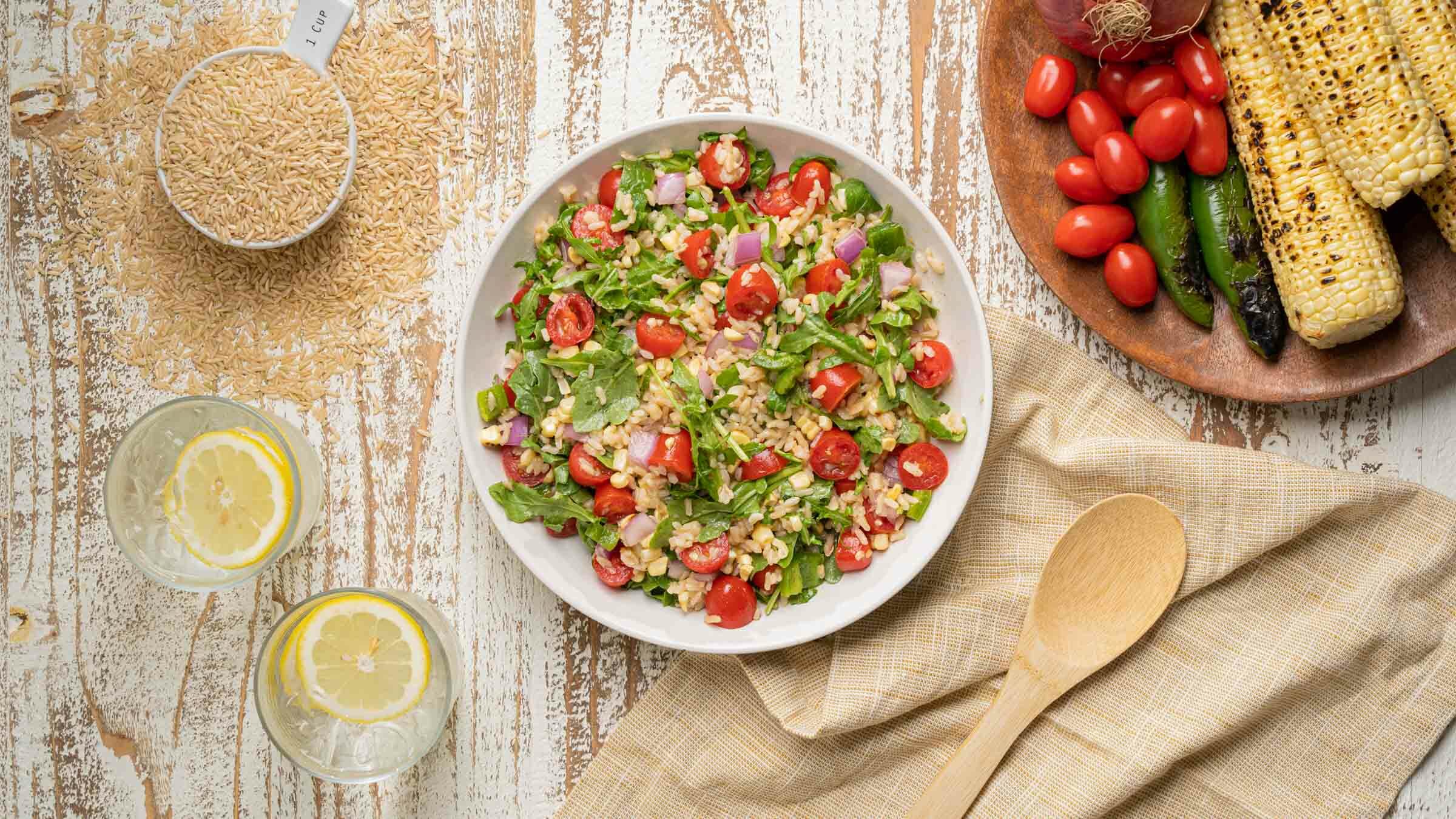 Summer Salad with corn, rice, onions, tomatoes and arugula in bowl.